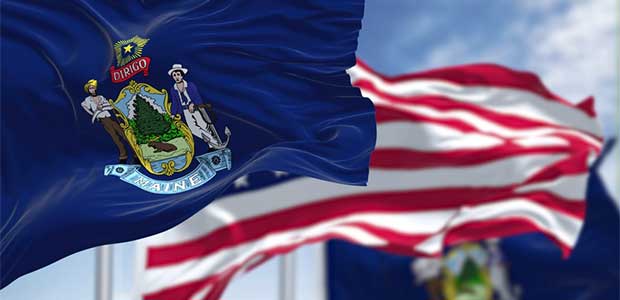 Flag of Maine flying in front of American flag. Behind the American flag is another flag of Maine