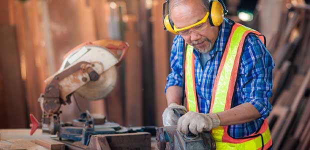 man wearing hearing, vision and hand protection while working sanding next to saw