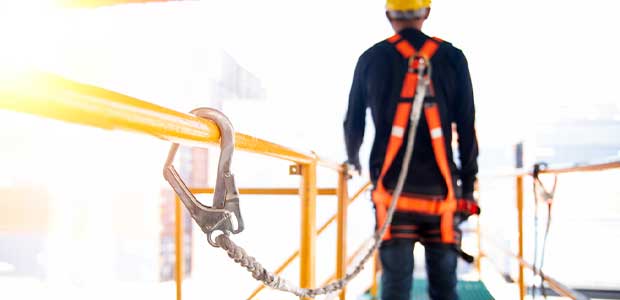 up-close view of fall protection clipped to bar with person dressed in fall protection in background