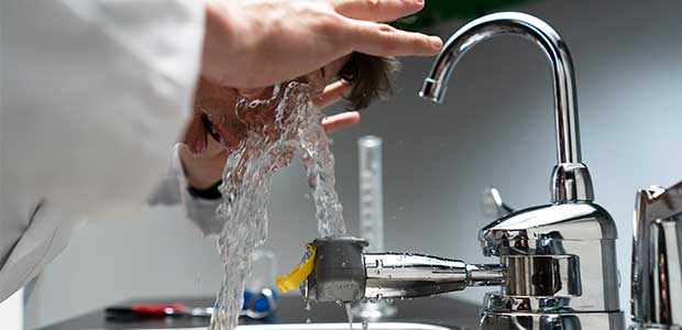 person washing eyes under an eyewash station attached to a sink
